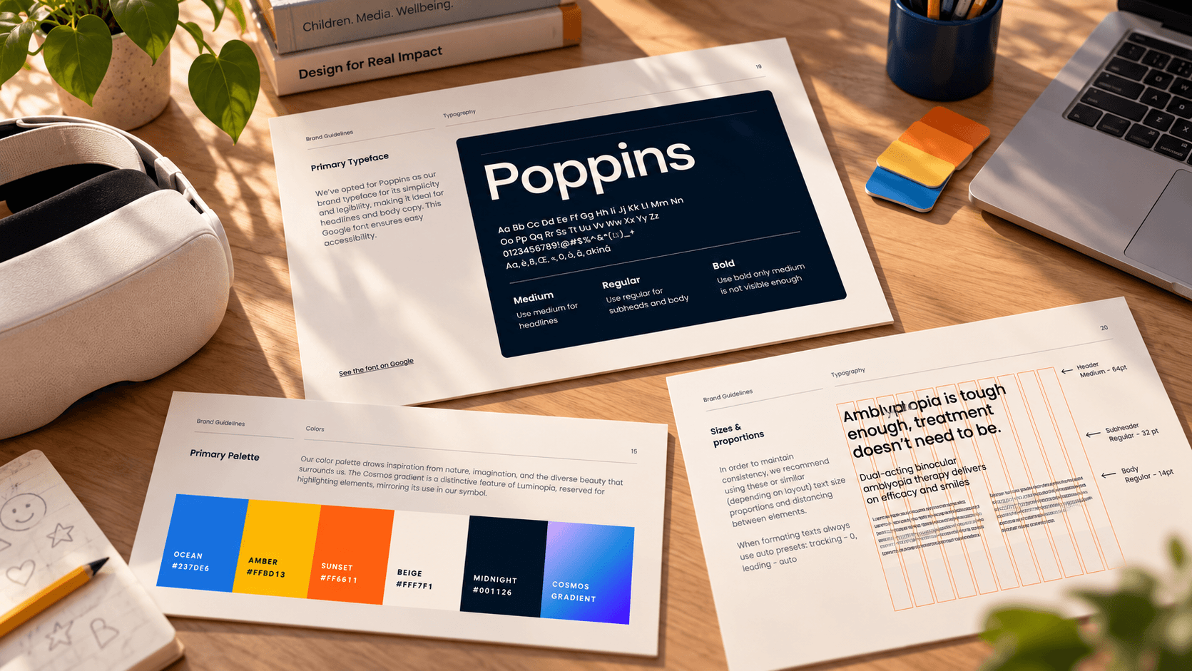 Luminopia's brand guide printed on a desk: Poppins in Medium, Regular and Bold, the type scale on a column grid, and the primary palette of Ocean, Amber, Sunset, Beige, Midnight and the Cosmos gradient, beside a VR headset and a laptop