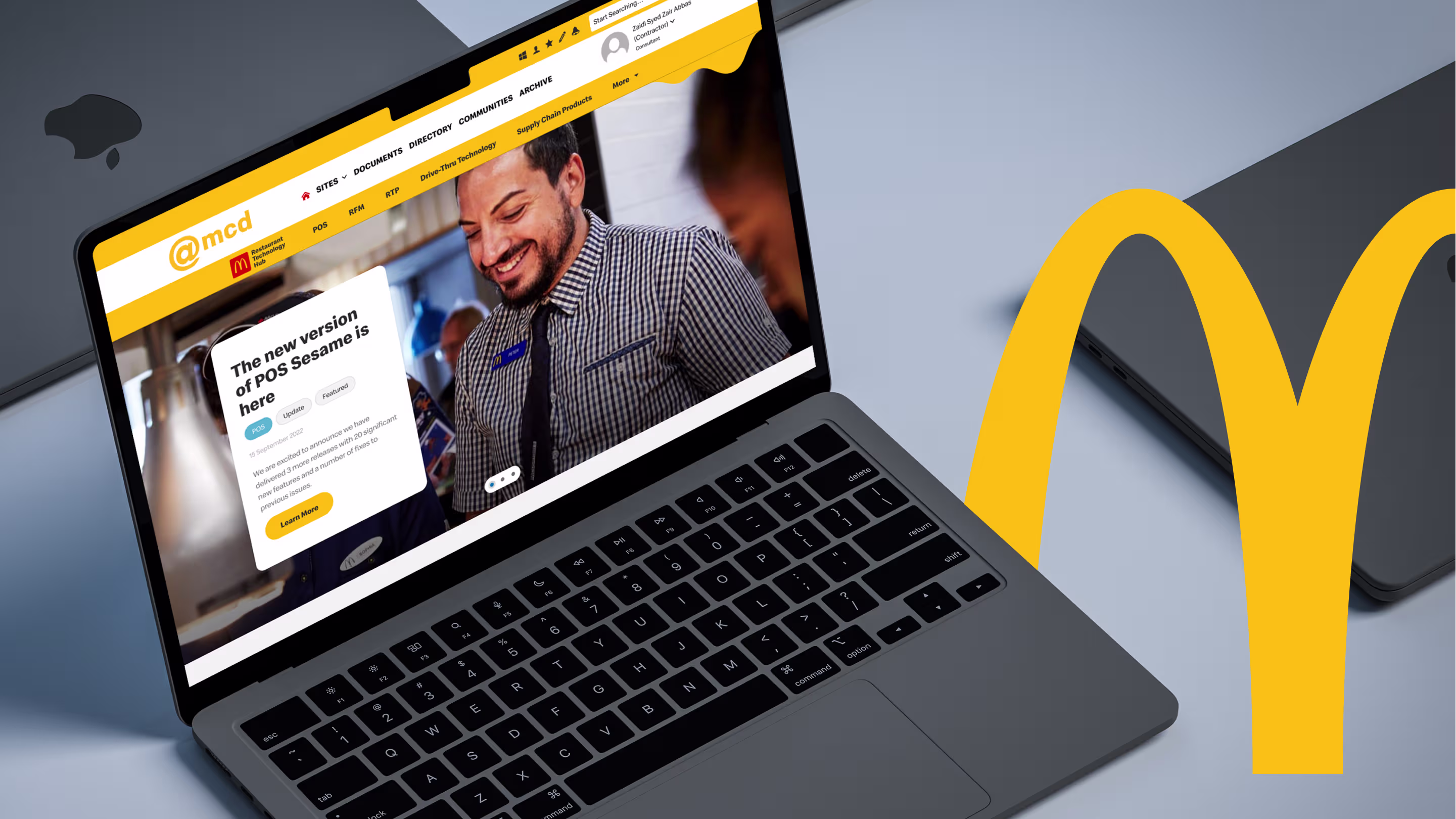 Laptop showing the Restaurant Technology Hub home page inside McDonald's @mcd intranet, beside a large golden arch